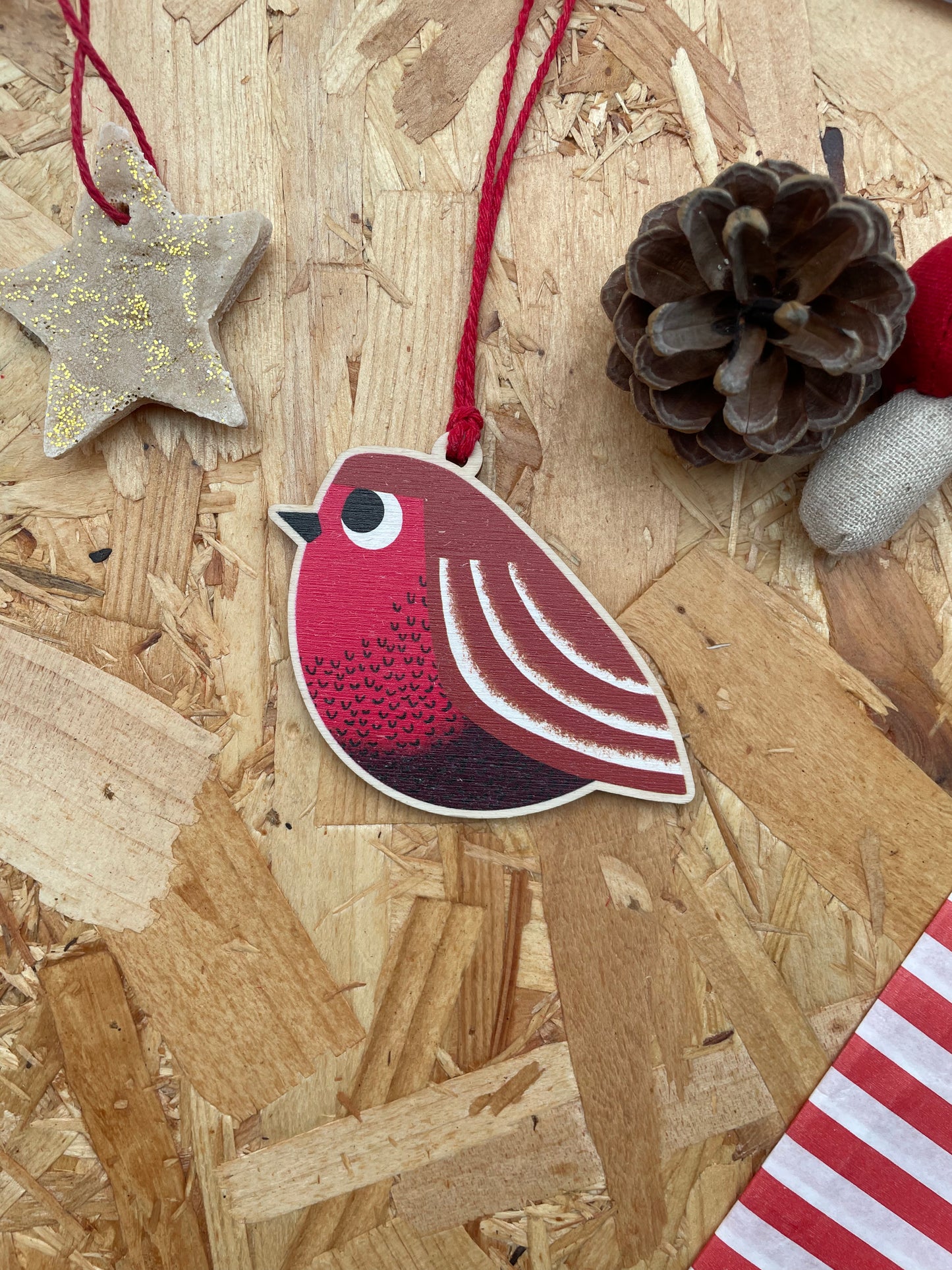 Decorative red robin ornament on a wooden surface with pine cones and a star.