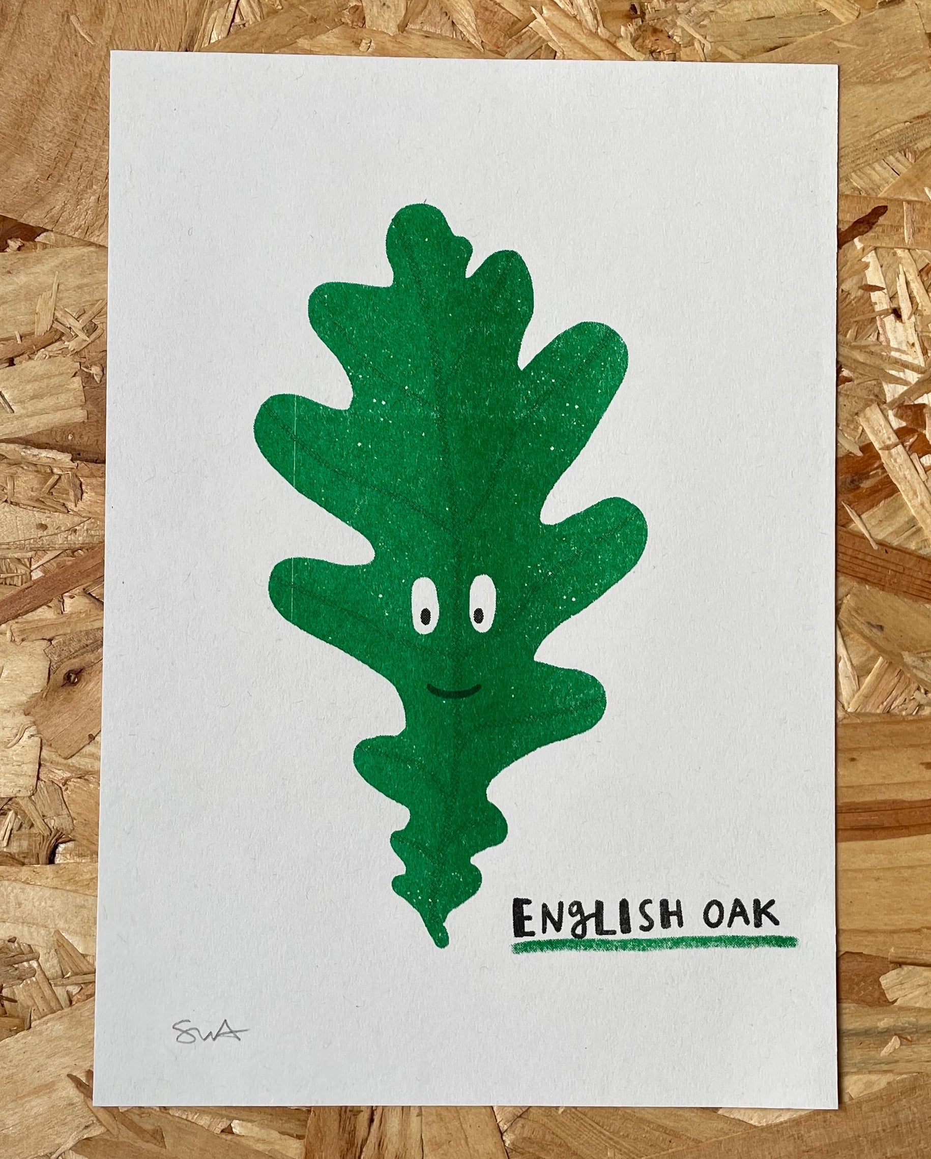 Risograph print of a green oak leaf character with eyes and a mouth on a white background, labeled 'English Oak', on a wooden surface.