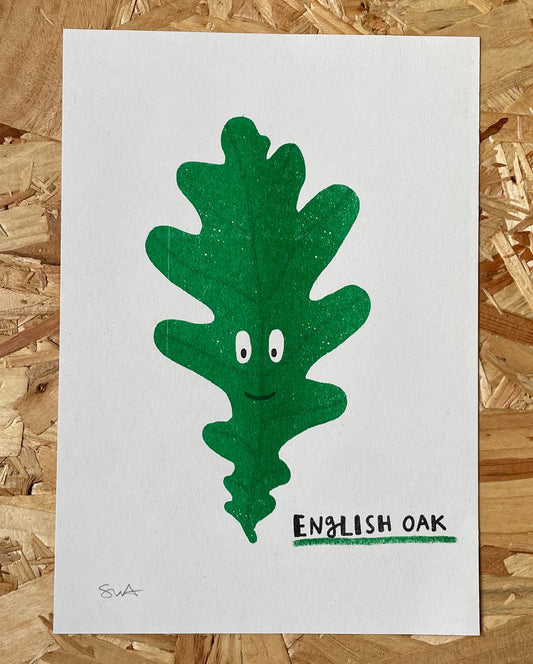 Risograph print of a green oak leaf character with eyes and a mouth on a white background, labeled 'English Oak', on a wooden surface.