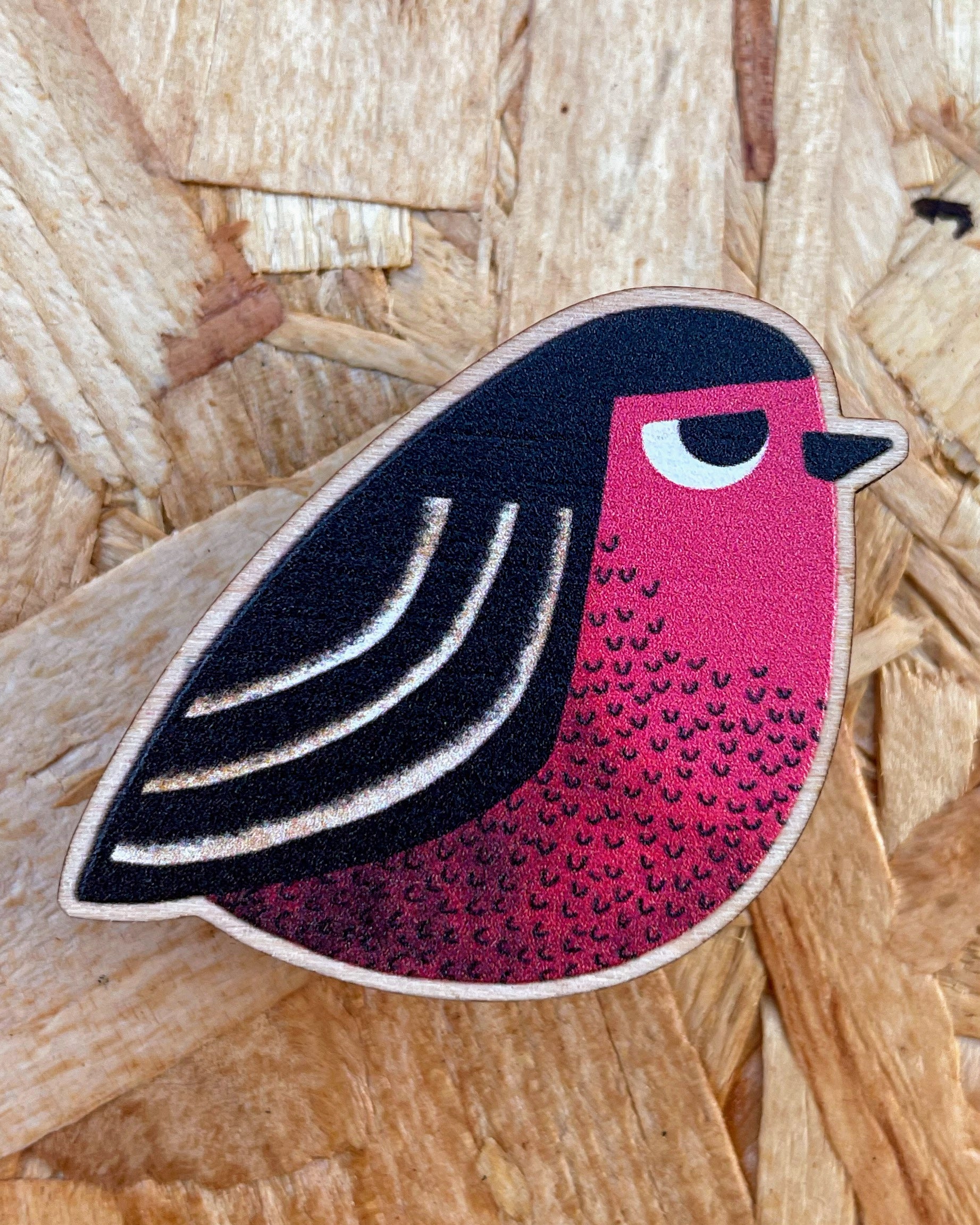 Robin Bird-shaped wooden pin badge with pink and black design on a wooden surface