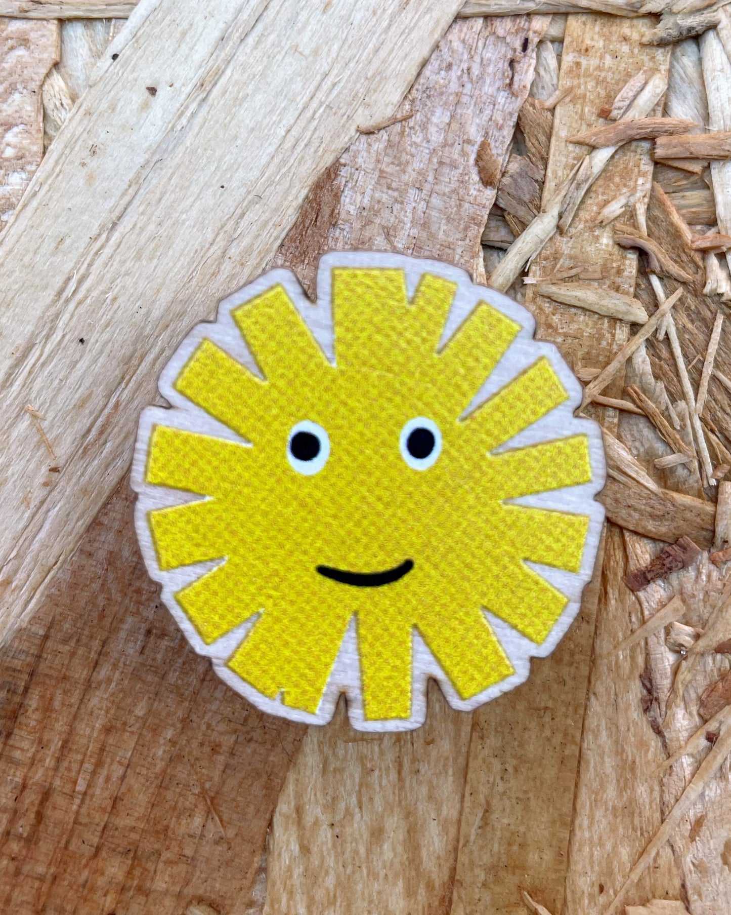Yellow sun-shaped brooch with a smiley face on a wooden surface