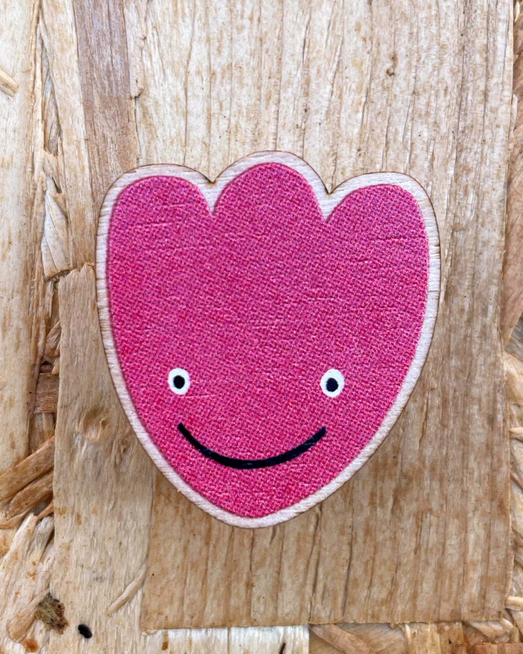 Pink tulip-shaped wooden pin badge with a smiley face on a wooden background.