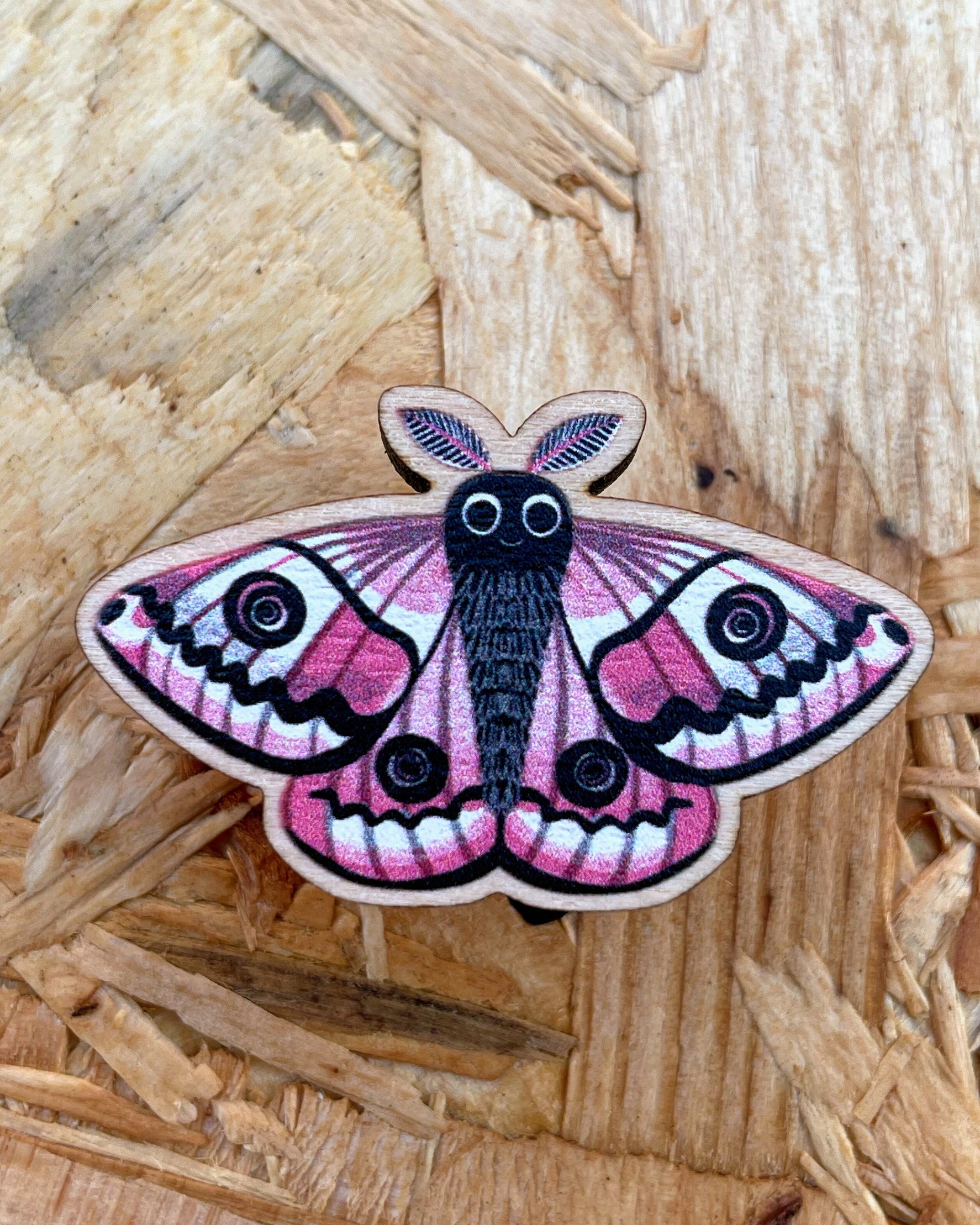 Close up of a quirky emperor moth wooden pin badge, on wooden background. 