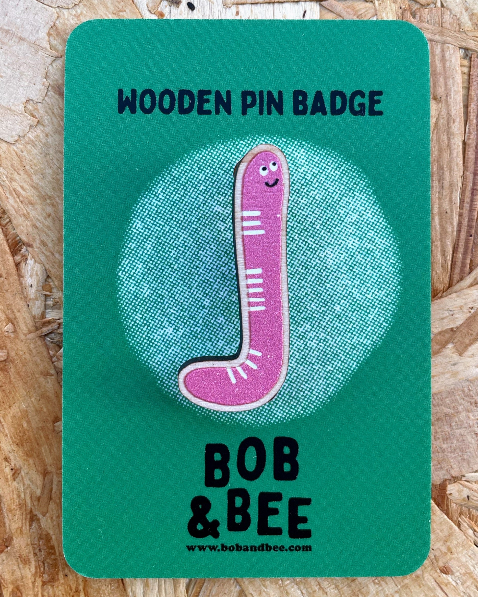Worm design - Wooden pin badge on a green card with 'Bob & Bee' branding. With a wooden background. 