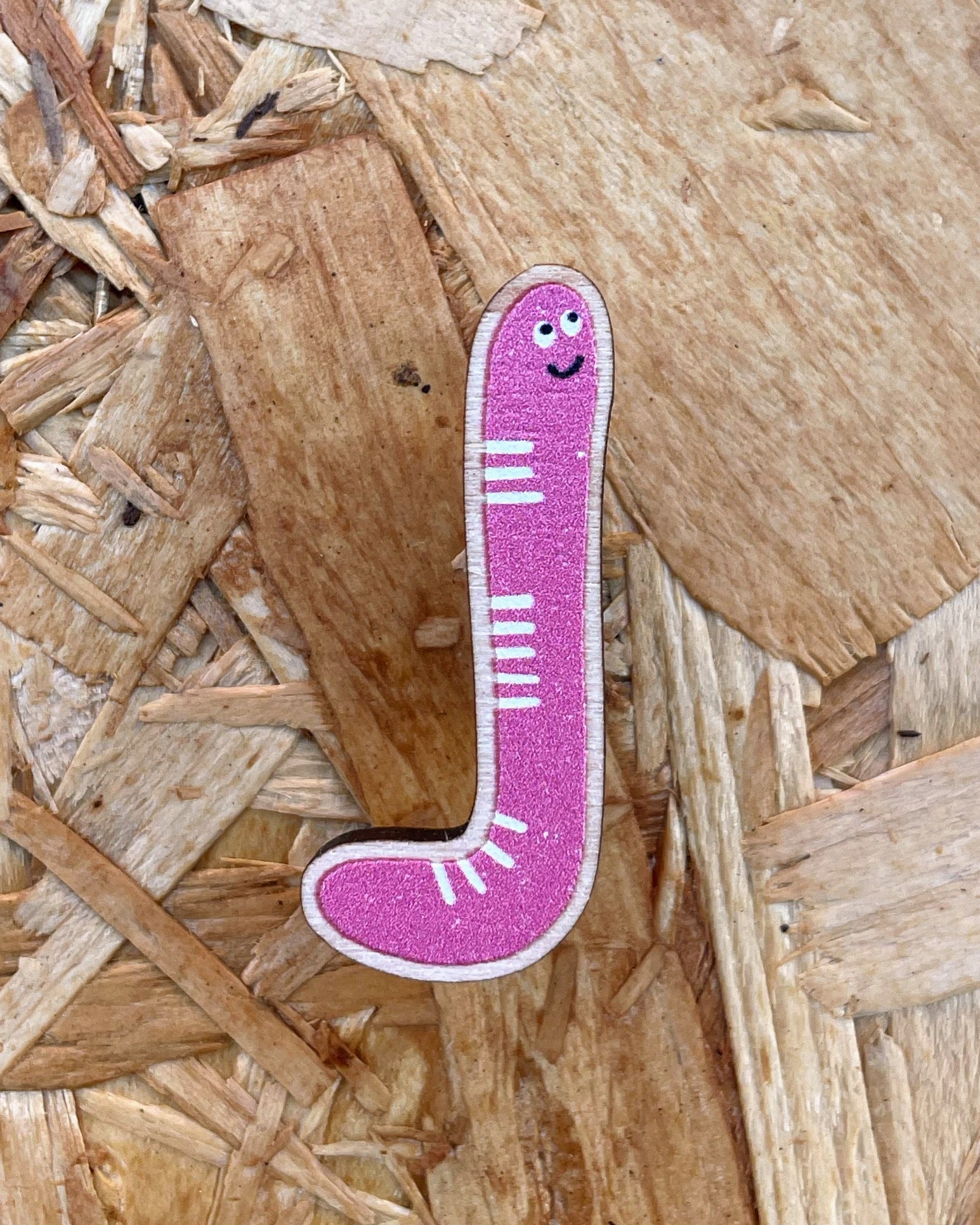 Pink worm wooden pin badge with a smiling face on a wooden surface